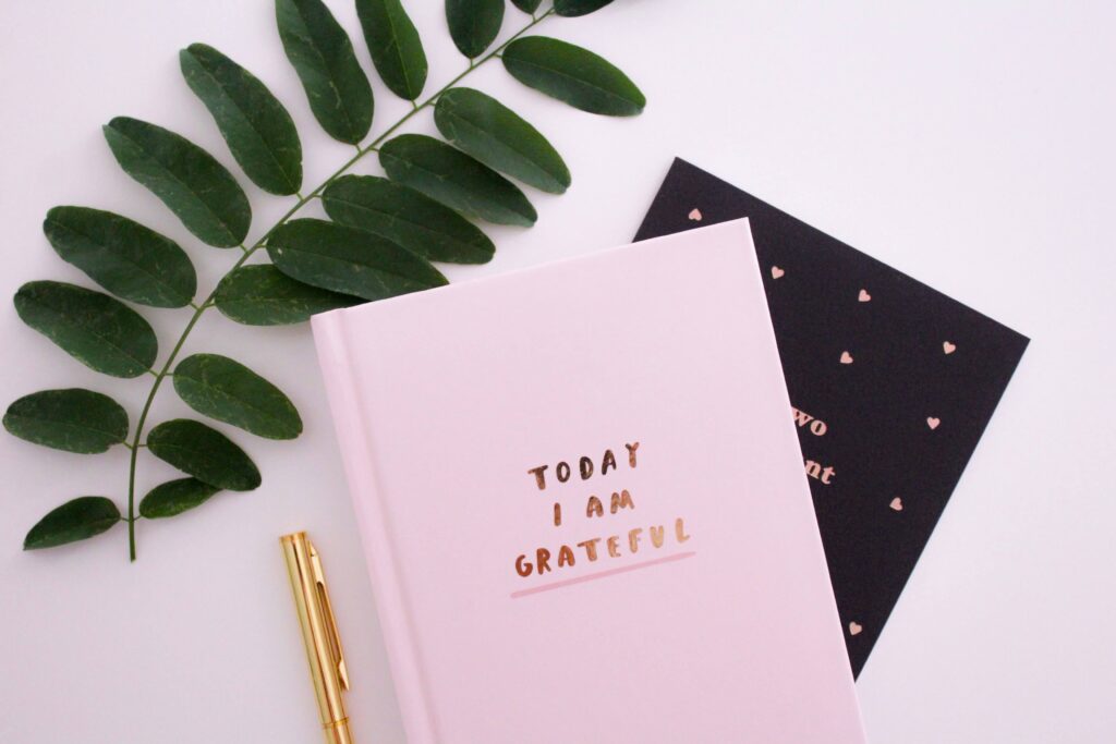 A pink gratitude journal with a gold pen. With the help of a women's therapist in NYC, NY, you can break free from the comparison trap! Contact me to begin women's issues therapy.