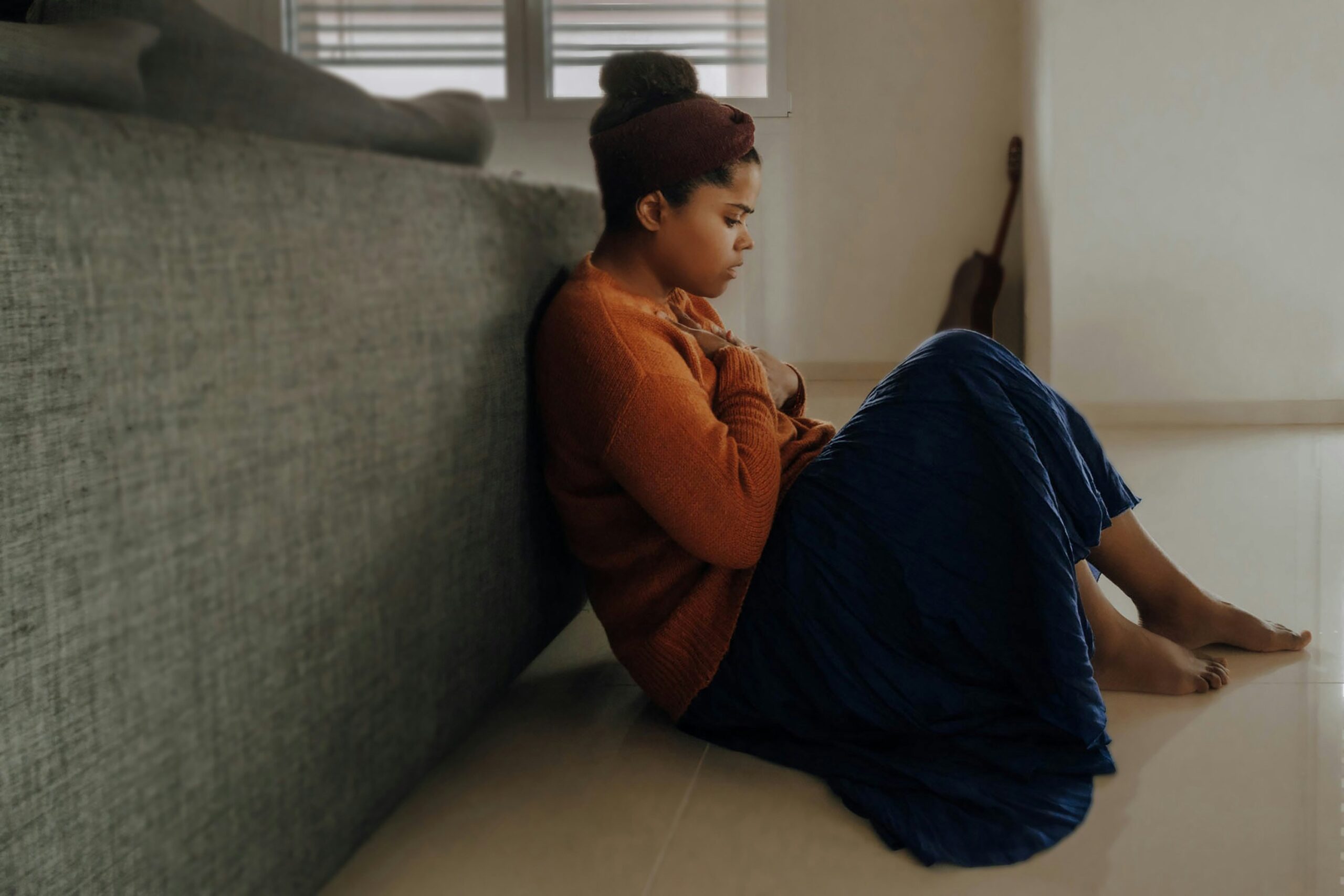 An individual sitting against a couch, representing anxiety & tension. With a women's therapist in NYC, NY, you can work to overcome your anxiety. Get started with a women's therapist today!