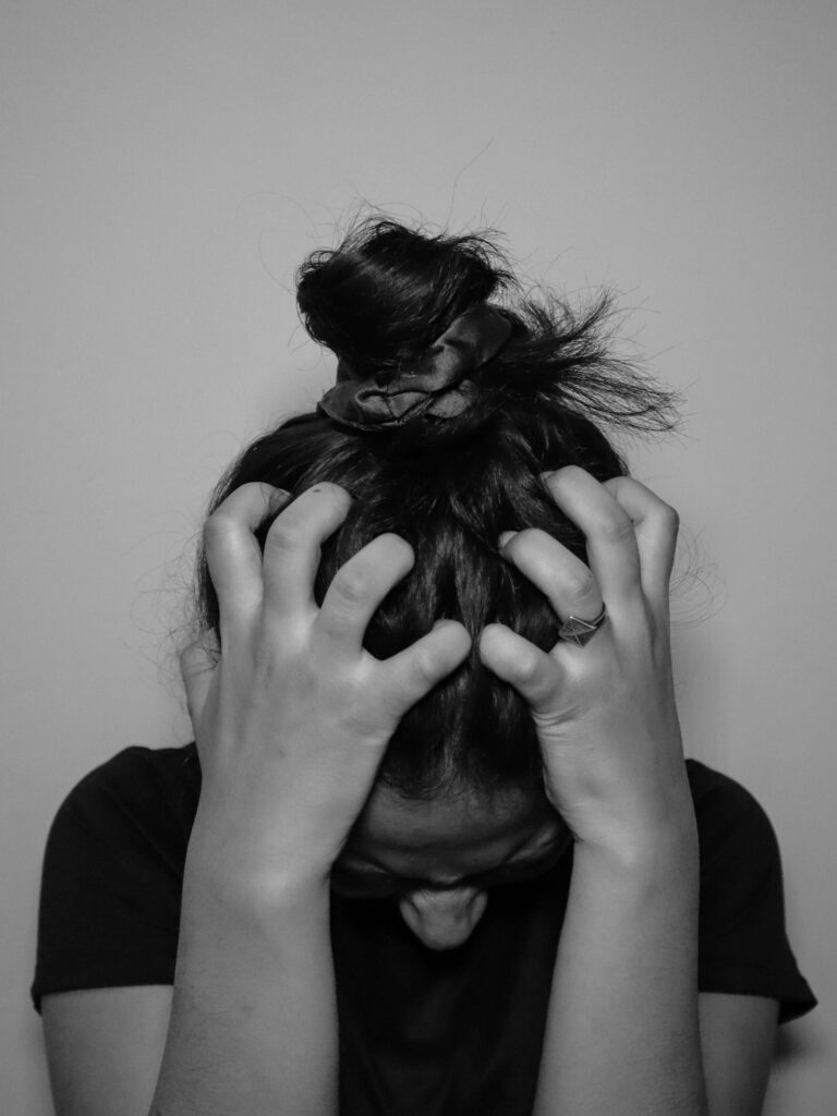A young woman with her hands pulling her hair. Representing how stress can be harmful to women's mental health. Begin working to heal with a women's therapist in New York City. 