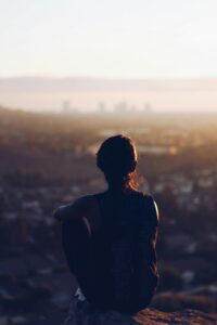 A woman looking at out at a city skyline while sitting on a mountain edge. If you struggle with the fear of failure, work with a therapist for women's issues in NYC, NY today. I can help you find coping skills for perfectionism.