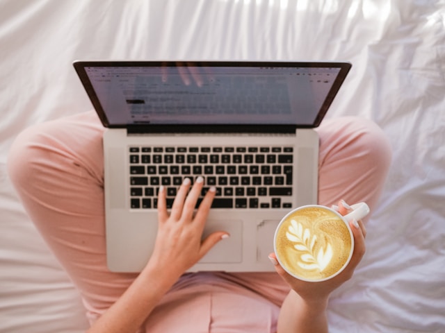 Woman typing on laptop in bed with coffee