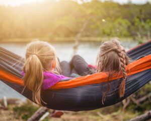 Two girls swinging in a hammock at summer camp. If your teen is headed to summer camp & homesick, develop strategies for managing it here! As a therapist for women's issues in Brooklyn, NY, I am here to help.