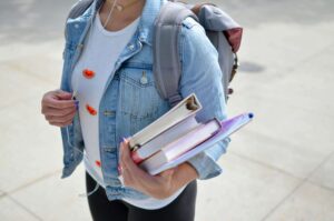 A college girl holding textbooks and a backpack. If the transition to college makes you feel anxious, contact me today! I offer therapy for women's issues in NYC, NY to help college transitions.
