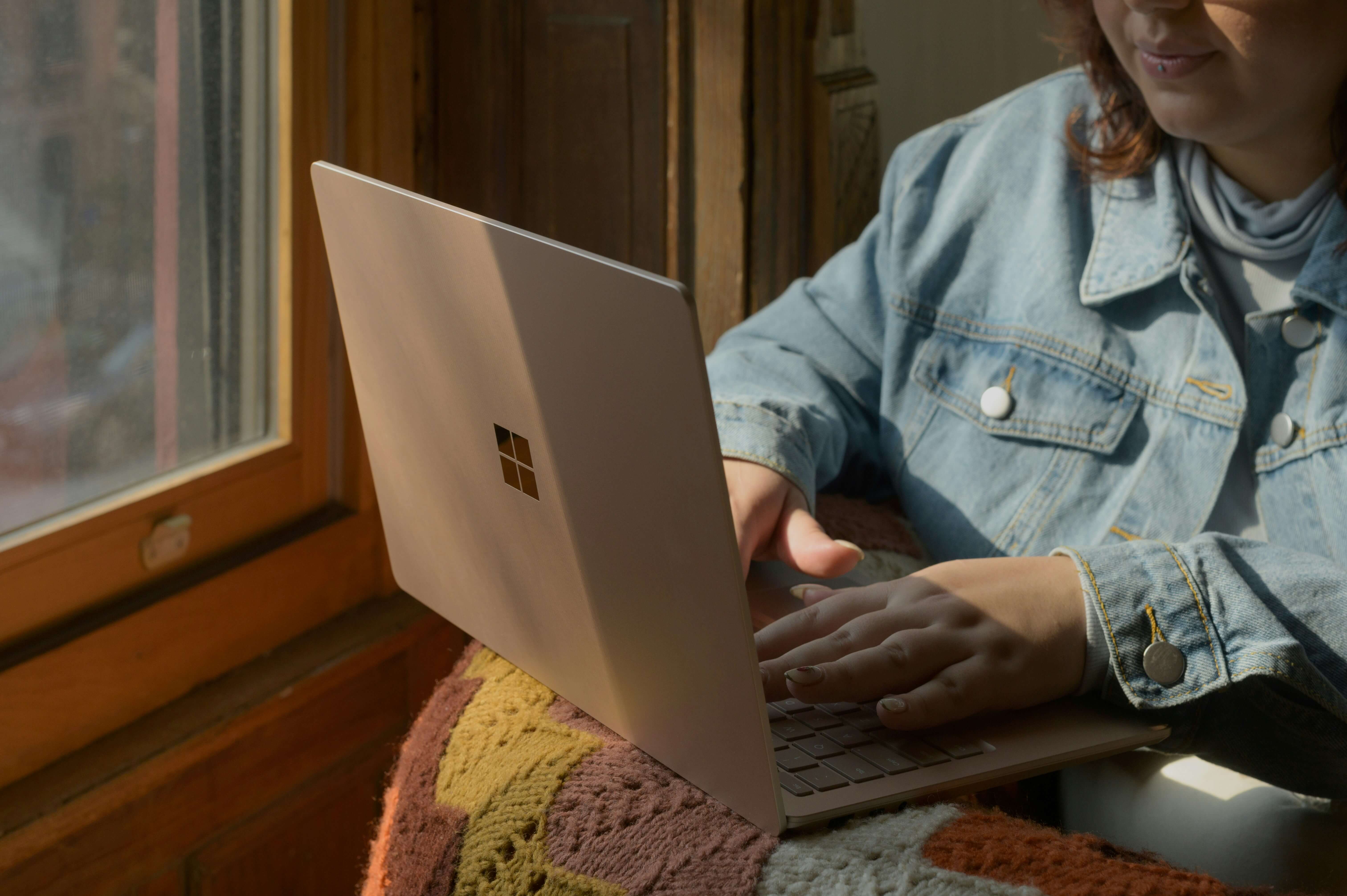A woman wearing a jean jacket typing on a laptop while sitting near a window. A women's therapist in NYC, NY can help support you. Start your healing journey today!